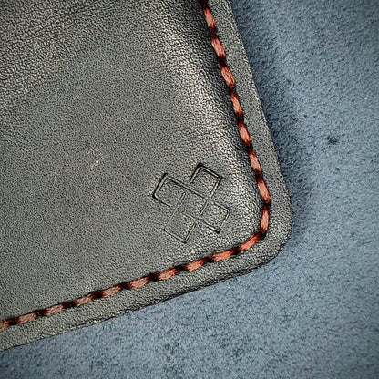 Back view close-up of the design logo emboss on the back of The Houdini card holder in vertical configuration– focusing on the fine grain detail of ethically sourced black full-grain leather and meticulous red saddle stitching. Showcases the subtle artistry and understated luxury of Novelty Atelier’s craftsmanship.
