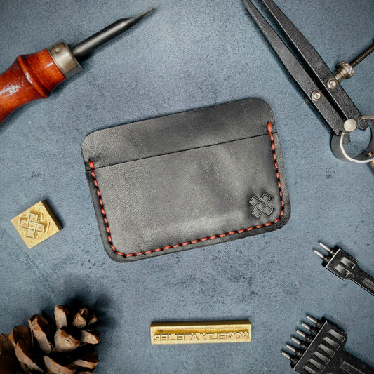 Back view of The Houdini minimalist leather card holder in horizontal configuration by Novelty Atelier – features a clean, functional layout with the design logo subtly stamped into black full-grain leather. Accented with red saddle stitching for a timeless aesthetic.
