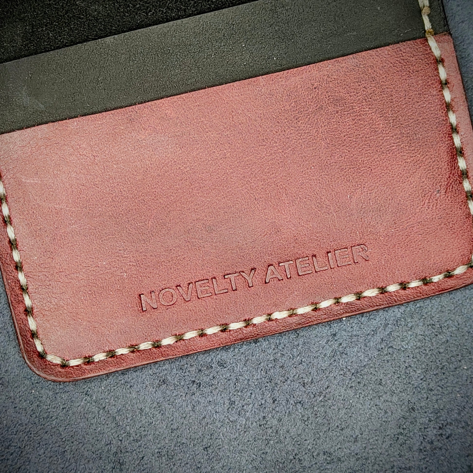 Close up of The Copperfield bifold card holder by Novelty Atelier detailed view of brand name logo embossed into Black and Purple full grain leather. Features precise saddle stitching in off white thread and hand finished edges. Symbol of artisanal craftsmanship and functional luxury.
