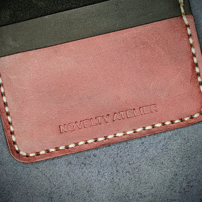 Close up of The Copperfield bifold card holder by Novelty Atelier detailed view of brand name logo embossed into Black and Purple full grain leather. Features precise saddle stitching in off white thread and hand finished edges. Symbol of artisanal craftsmanship and functional luxury.
