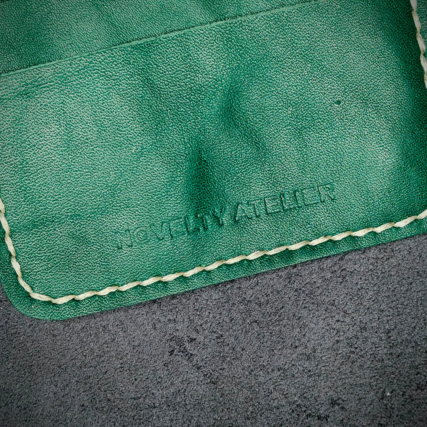 Close up of The Copperfield bifold card holder by Novelty Atelier detailed view of brand name logo embossed into Green full grain leather. Features precise saddle stitching in off white thread and hand finished edges. Symbol of artisanal craftsmanship and functional luxury.
