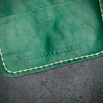 Close up of The Copperfield bifold card holder by Novelty Atelier detailed view of brand name logo embossed into Green full grain leather. Features precise saddle stitching in off white thread and hand finished edges. Symbol of artisanal craftsmanship and functional luxury.
