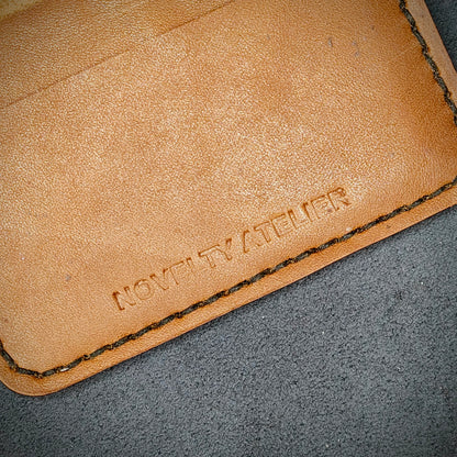Close up of The Copperfield bifold card holder by Novelty Atelier detailed view of brand name logo embossed into Tann full grain leather. Features precise saddle stitching in black thread and hand finished edges. Symbol of artisanal craftsmanship and functional luxury.
