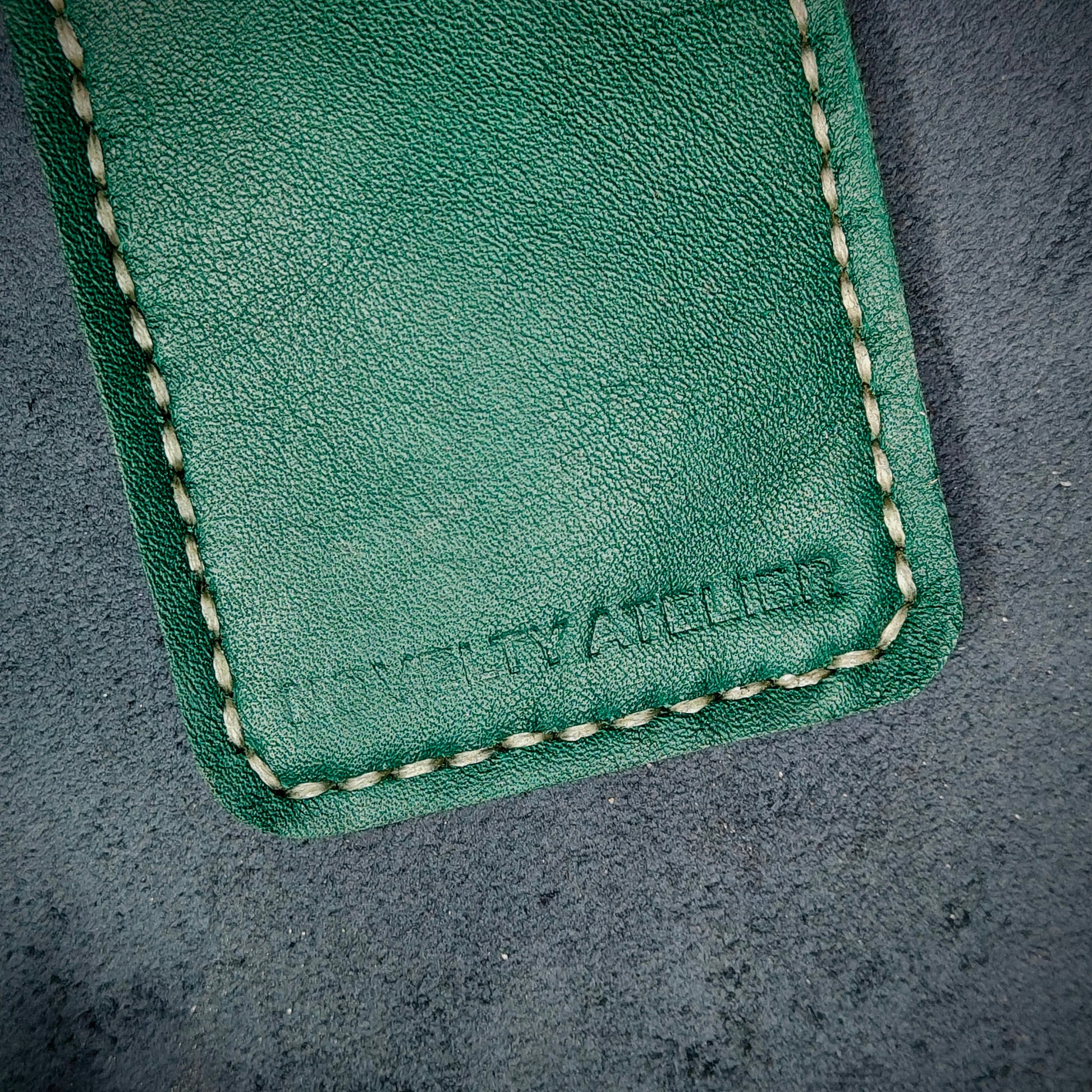 Front view close up shot of the Novelty Atelier brand emboss on The Houdini card holder – detailed close-up of premium black and green full-grain leather and contrast off white hand-stitching . Emphasizes the sharp, elegant logo impression and tactile texture, appealing to luxury EDC and minimalist gear collectors.
