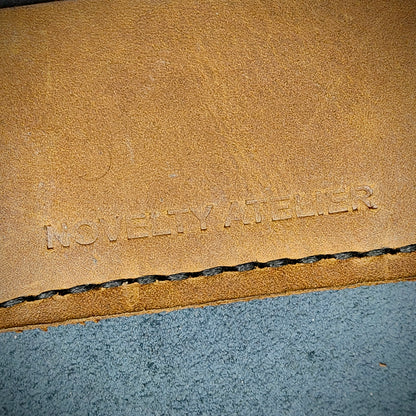 Front view close up shot of the Novelty Atelier brand emboss on The Houdini card holder – detailed close-up of premium black and sandstorm Brown full-grain leather and contrast black hand-stitching . Emphasizes the sharp, elegant logo impression and tactile texture, appealing to luxury EDC and minimalist gear collectors.
