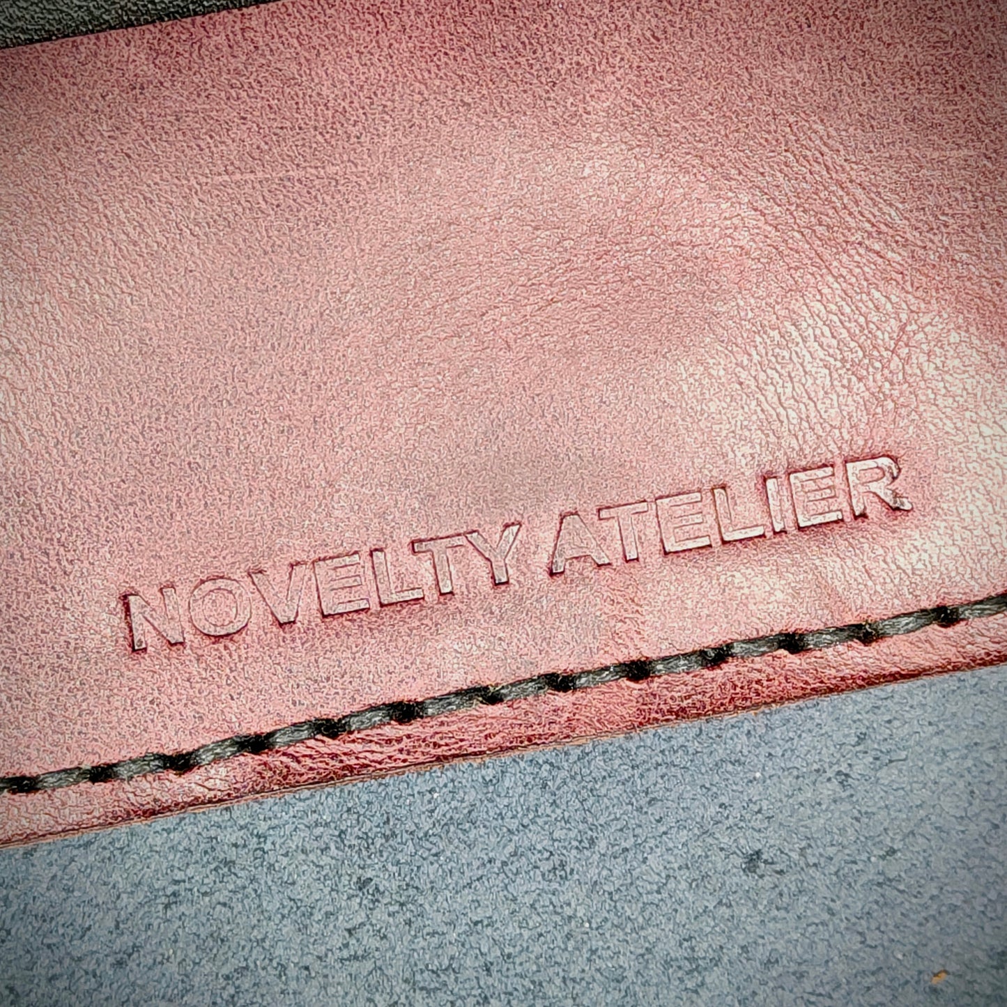 Front view close up shot of the Novelty Atelier brand emboss on The Houdini card holder horizontal configuration– detailed close-up of premium Black and Purple full-grain leather and contrast Black hand-stitching . Emphasizes the sharp, elegant logo impression and tactile texture, appealing to luxury EDC and minimalist gear collectors.
