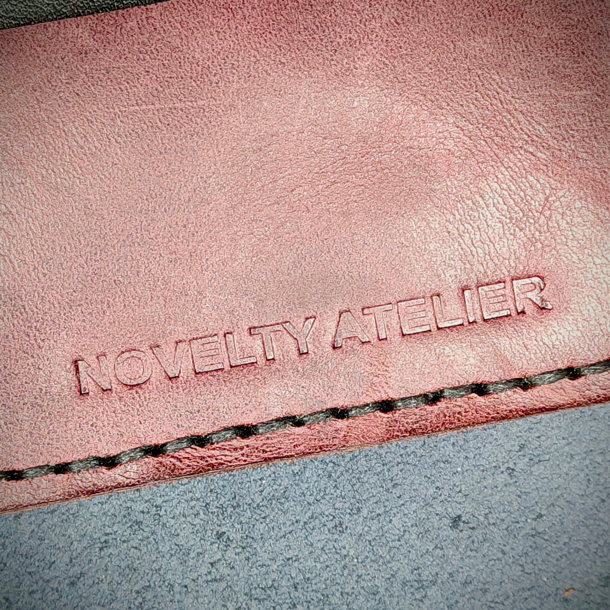 Front view close up shot of the Novelty Atelier brand emboss on The Houdini card holder horizontal configuration– detailed close-up of premium Black and Purple full-grain leather and contrast Black hand-stitching . Emphasizes the sharp, elegant logo impression and tactile texture, appealing to luxury EDC and minimalist gear collectors.
