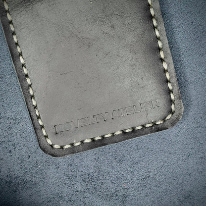 Front view close up shot of the Novelty Atelier brand emboss on The Houdini card holder in vertical configuration– detailed close-up of premium Black full-grain leather and contrast off-white hand-stitching . Emphasizes the sharp, elegant logo impression and tactile texture, appealing to luxury EDC and minimalist gear collectors.
