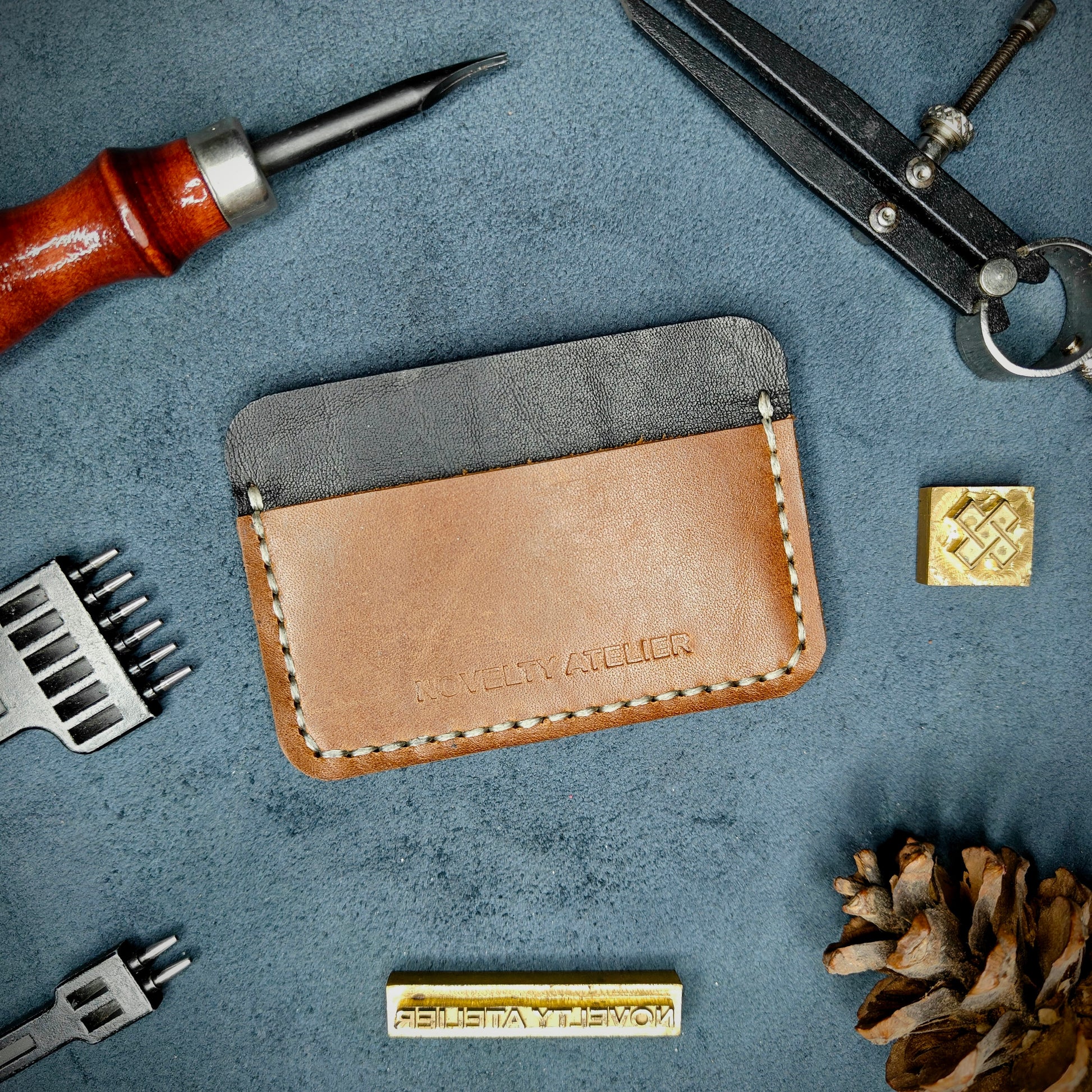 Front view of The Houdini minimalist card holder in horizontal configuration by Novelty Atelier – handcrafted from Black and Brown ethically sourced full-grain leather with contrasting off-white saddle stitching. Features the “Novelty Atelier” brand name cleanly embossed on the front. Perfectly balanced minimalist wallet design tailored for modern EDC enthusiasts who value craftsmanship and brand integrity.
