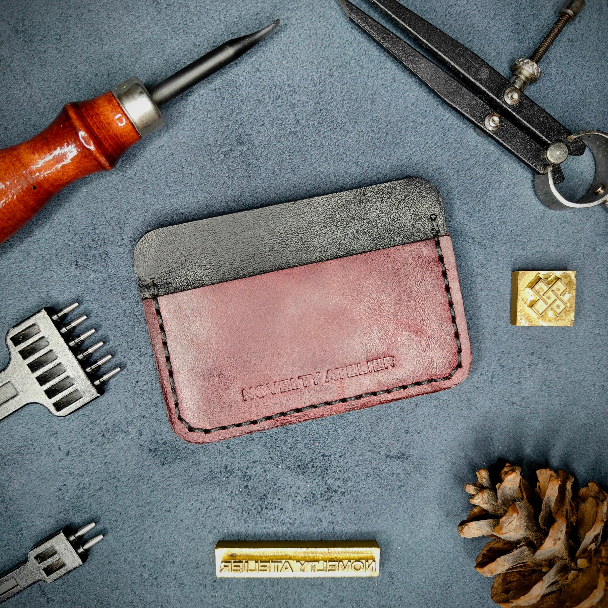 Front view of The Houdini minimalist card holder in horizontal configuration by Novelty Atelier – handcrafted from Black and Purple ethically sourced full-grain leather with crisp Black saddle stitching. Features the “Novelty Atelier” brand name cleanly embossed on the front. Perfectly balanced minimalist wallet design tailored for modern EDC enthusiasts who value craftsmanship and brand integrity.

