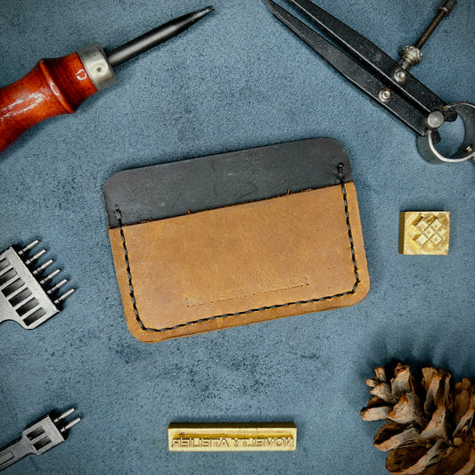 Front view of The Houdini minimalist card holder in horizontal configuration by Novelty Atelier – handcrafted from Black and sandstorm brown ethically sourced full-grain leather with crisp black saddle stitching. Features the “Novelty Atelier” brand name cleanly embossed on the front. Perfectly balanced minimalist wallet design tailored for modern EDC enthusiasts who value craftsmanship and brand integrity.
