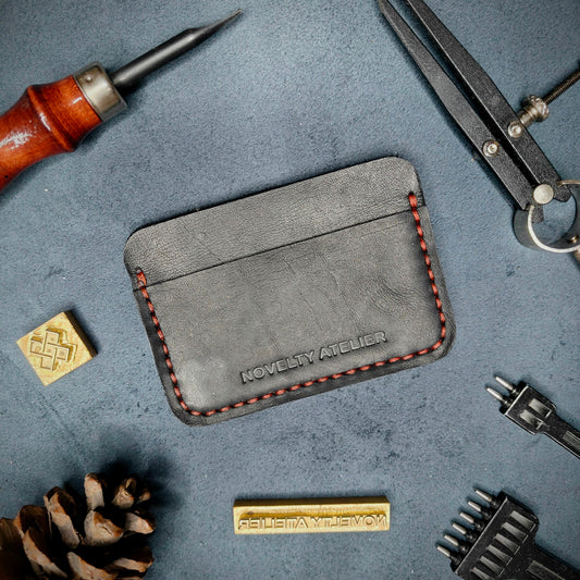Front view of The Houdini minimalist card holder in horizontal configuration by Novelty Atelier – handcrafted from Black ethically sourced full-grain leather with contrasting  red saddle stitching. Features the “Novelty Atelier” brand name cleanly embossed on the front. Perfectly balanced minimalist wallet design tailored for modern EDC enthusiasts who value craftsmanship and brand integrity.