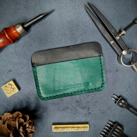 Front view of The Houdini minimalist card holder in horizontal configuration by Novelty Atelier – handcrafted from black and green ethically sourced full-grain leather with crisp black saddle stitching. Features the “Novelty Atelier” brand name cleanly embossed on the front. Perfectly balanced minimalist wallet design tailored for modern EDC enthusiasts who value craftsmanship and brand integrity.
