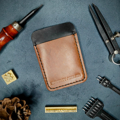 Front view of The Houdini minimalist card holder in vertical configuration by Novelty Atelier – handcrafted from Black and Brown ethically sourced full-grain leather with contrasting Black saddle stitching. Features the “Novelty Atelier” brand name cleanly embossed on the front. Perfectly balanced minimalist wallet design tailored for modern EDC enthusiasts who value craftsmanship and brand integrity.
