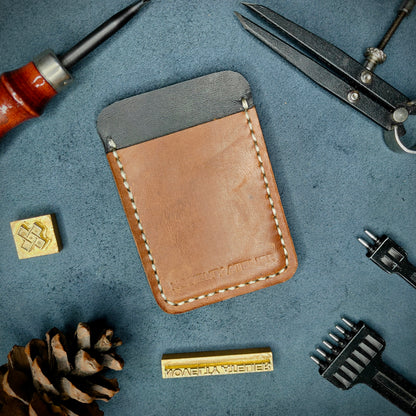 Front view of The Houdini minimalist card holder in vertical configuration by Novelty Atelier – handcrafted from Black and Brown ethically sourced full-grain leather with contrasting off-white saddle stitching. Features the “Novelty Atelier” brand name cleanly embossed on the front. Perfectly balanced minimalist wallet design tailored for modern EDC enthusiasts who value craftsmanship and brand integrity.
