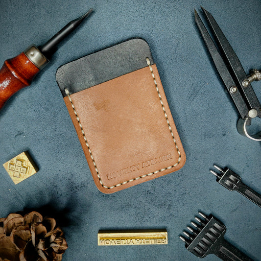 Front view of The Houdini minimalist card holder in vertical configuration by Novelty Atelier – handcrafted from Black and Tann ethically sourced full-grain leather with contrasting off-white saddle stitching. Features the “Novelty Atelier” brand name cleanly embossed on the front. Perfectly balanced minimalist wallet design tailored for modern EDC enthusiasts who value craftsmanship and brand integrity.