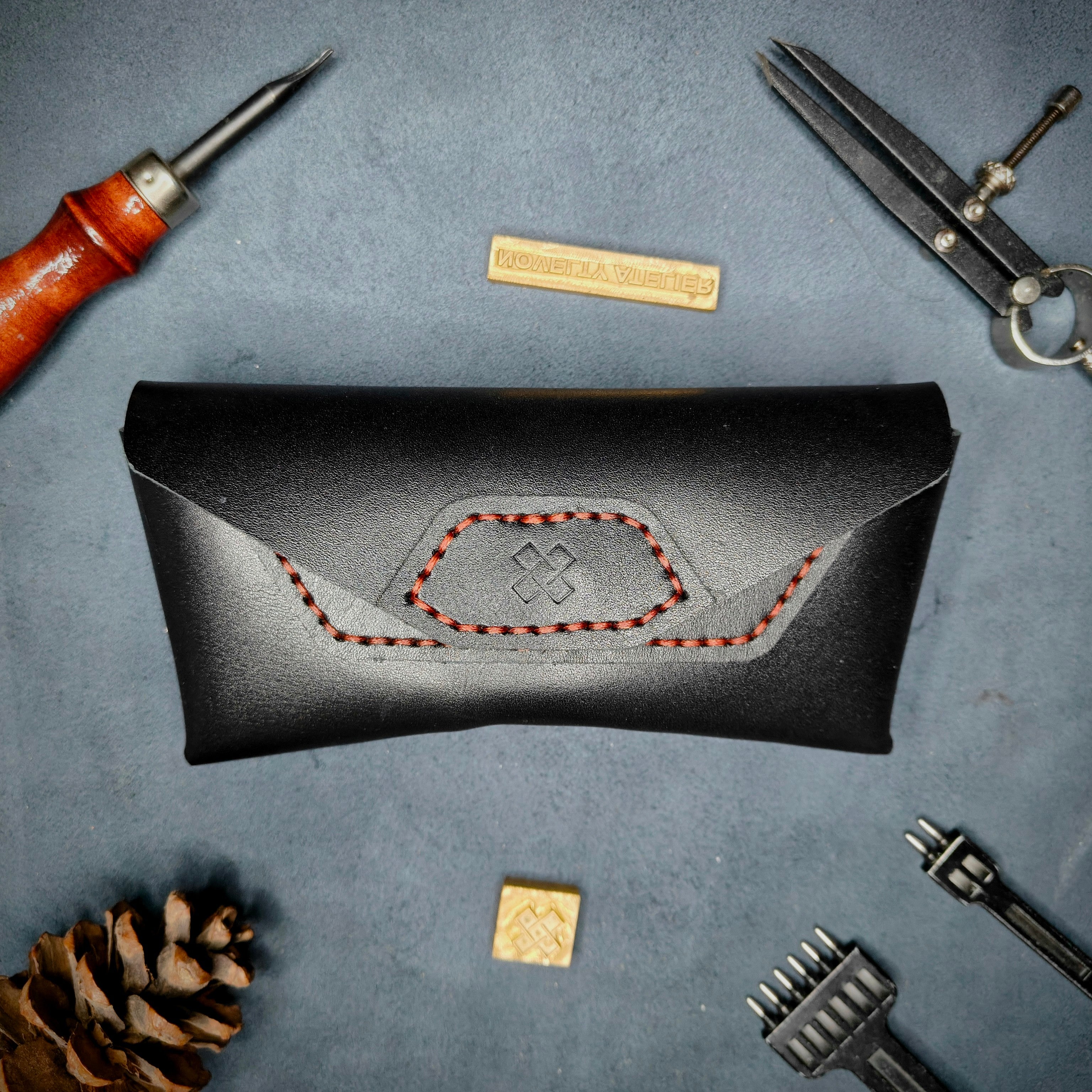 Home page Banner -The Hustler sunglass case - black leather with red thread - showing a detailed picture of the brand Logo Novelty Atelier - with all tools for aesthetics