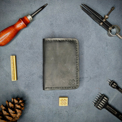The Copperfield full grain leather bifold wallet by Novelty Atelier closed view highlighting slim and rugged design. Handcrafted from Black and Mustard yellow ethically sourced leather, saddle stitched in black thread. Set against a textured background with branding tools and pine cone, perfect for minimalist EDC style.
