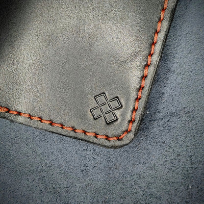Zoomed in view of Novelty Atelier’s signature insignia embossed on The Copperfield minimalist leather card holder. Hand stitched in Red thread using traditional saddle technique. Crafted from Black full grain leather, symbolizing timeless durability and ethical sophistication.

