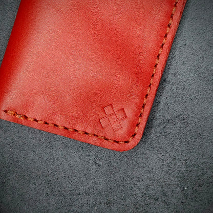 Zoomed in view of Novelty Atelier’s signature insignia embossed on The Copperfield minimalist leather card holder. Hand stitched in Red thread using traditional saddle technique. Crafted from Red full grain leather, symbolizing timeless durability and ethical sophistication.
