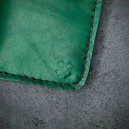 Zoomed in view of Novelty Atelier’s signature insignia embossed on The Copperfield minimalist leather card holder. Hand stitched in black thread using traditional saddle technique. Crafted from Green full grain leather, symbolizing timeless durability and ethical sophistication.
