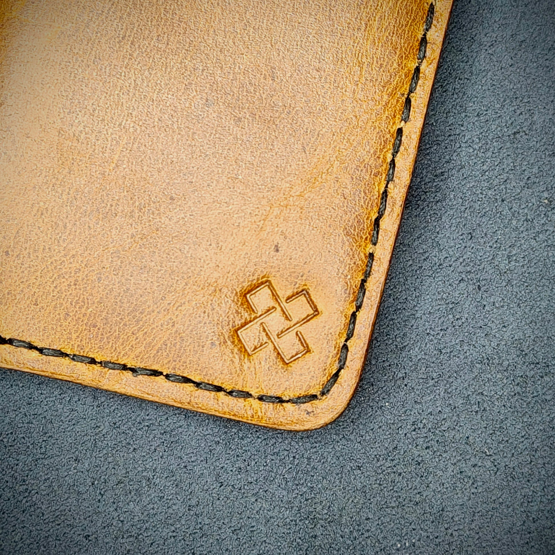 Zoomed in view of Novelty Atelier’s signature insignia embossed on The Copperfield minimalist leather card holder. Hand stitched in black thread using traditional saddle technique. Crafted from Mustard yellow full grain leather, symbolizing timeless durability and ethical sophistication.
