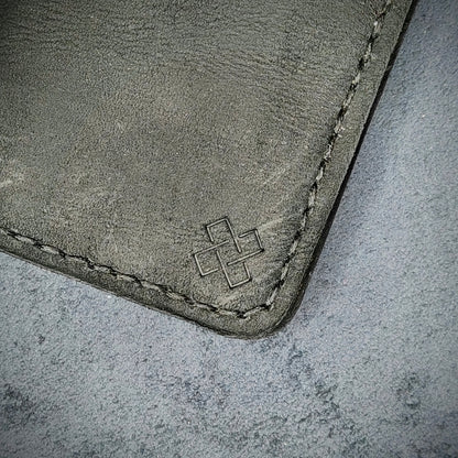 Zoomed in view of Novelty Atelier’s signature insignia embossed on The Copperfield minimalist leather card holder. Hand stitched in black thread using traditional saddle technique. Crafted from full grain Black and Brown leather, symbolizing timeless durability and ethical sophistication.