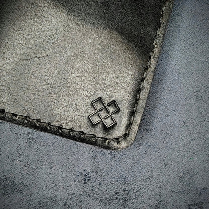 Zoomed in view of Novelty Atelier’s signature insignia embossed on The Copperfield minimalist leather card holder. Hand stitched in black thread using traditional saddle technique. Crafted from full grain Black and Green leather, symbolizing timeless durability and ethical sophistication.
