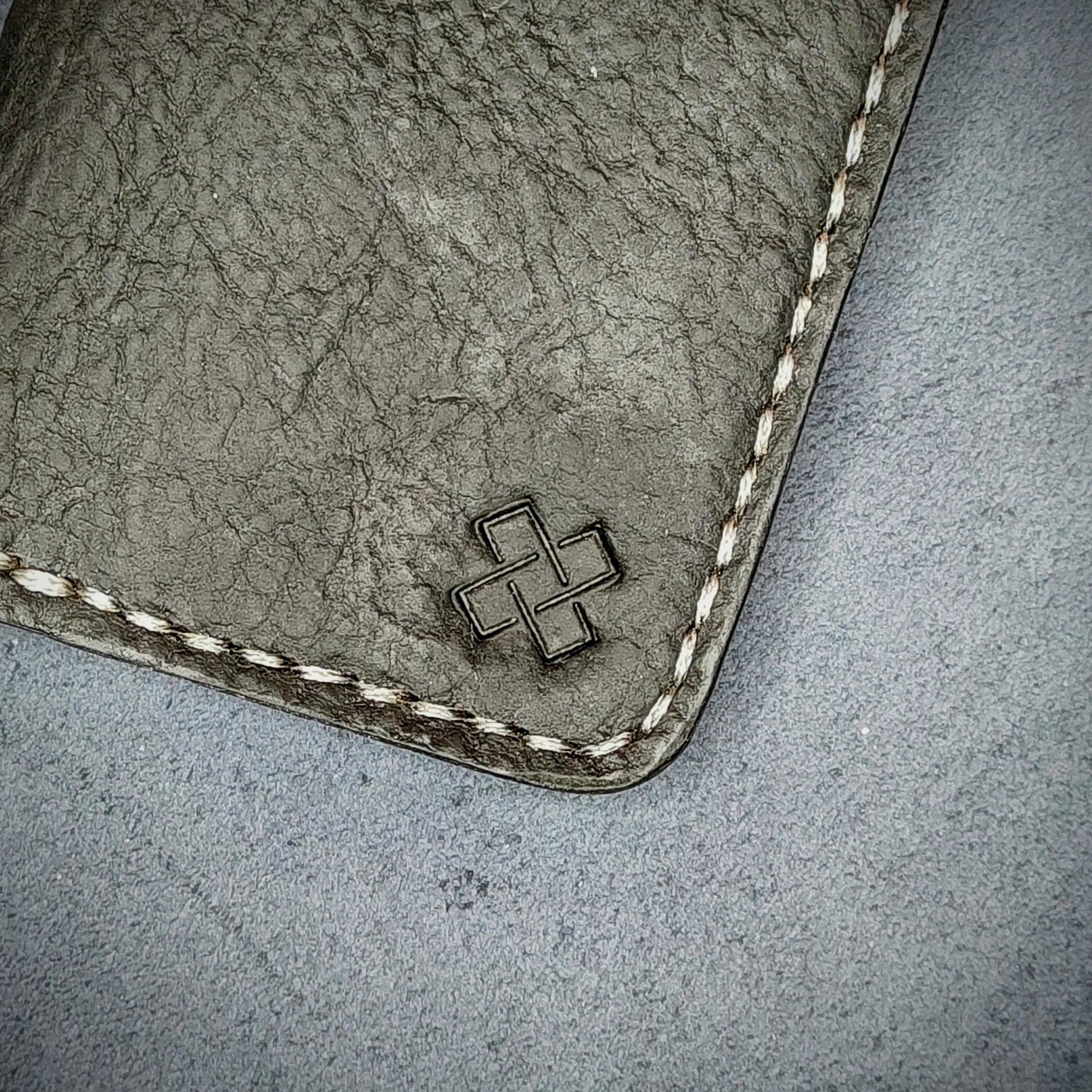 Zoomed in view of Novelty Atelier’s signature insignia embossed on The Copperfield minimalist leather card holder. Hand stitched in off white  thread using traditional saddle technique. Crafted from Black full grain leather, symbolizing timeless durability and ethical sophistication.

