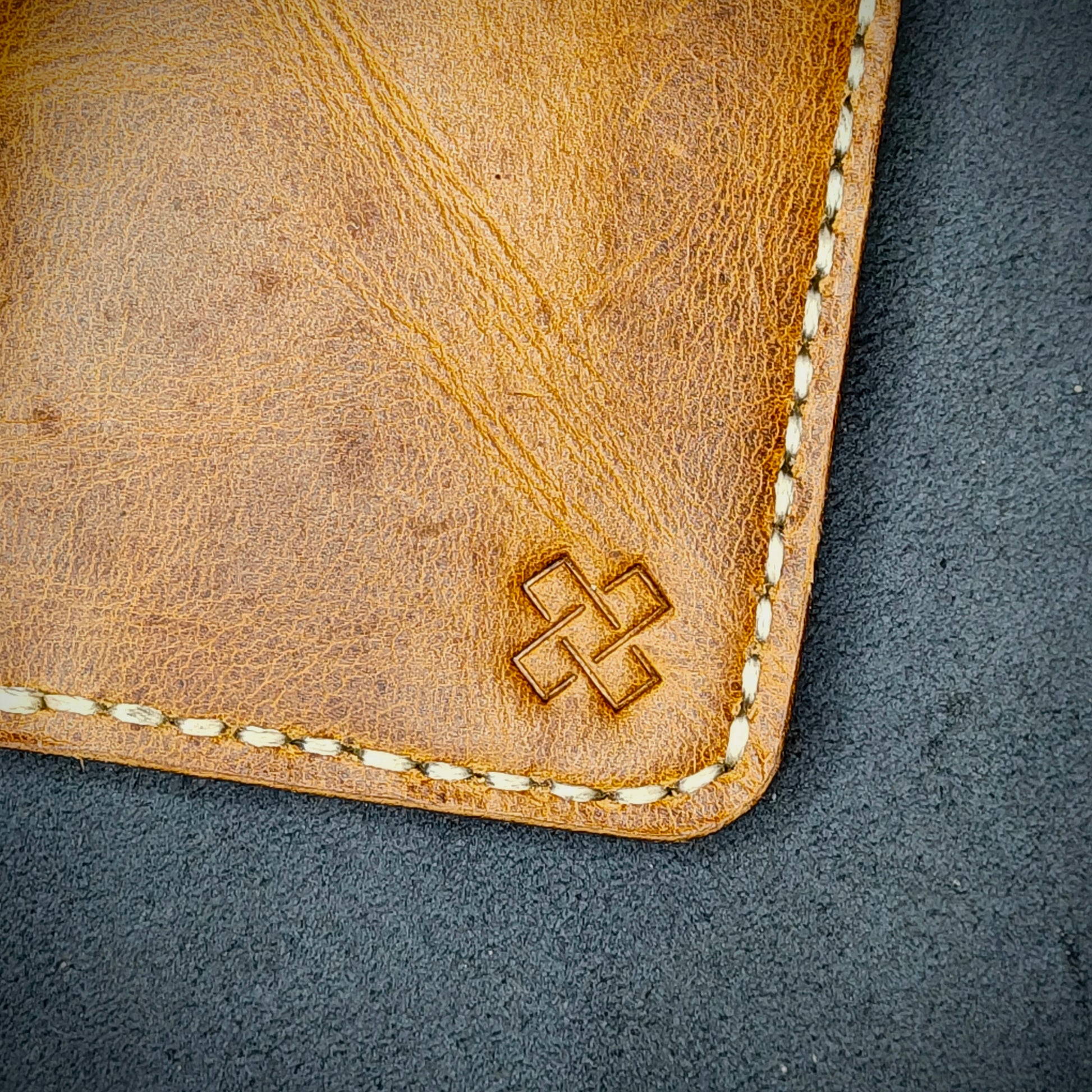 Zoomed in view of Novelty Atelier’s signature insignia embossed on The Copperfield minimalist leather card holder. Hand stitched in off white  thread using traditional saddle technique. Crafted from Mustard yellow full grain leather, symbolizing timeless durability and ethical sophistication.
