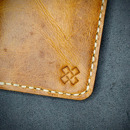 Zoomed in view of Novelty Atelier’s signature insignia embossed on The Copperfield minimalist leather card holder. Hand stitched in off white  thread using traditional saddle technique. Crafted from Mustard yellow full grain leather, symbolizing timeless durability and ethical sophistication.
