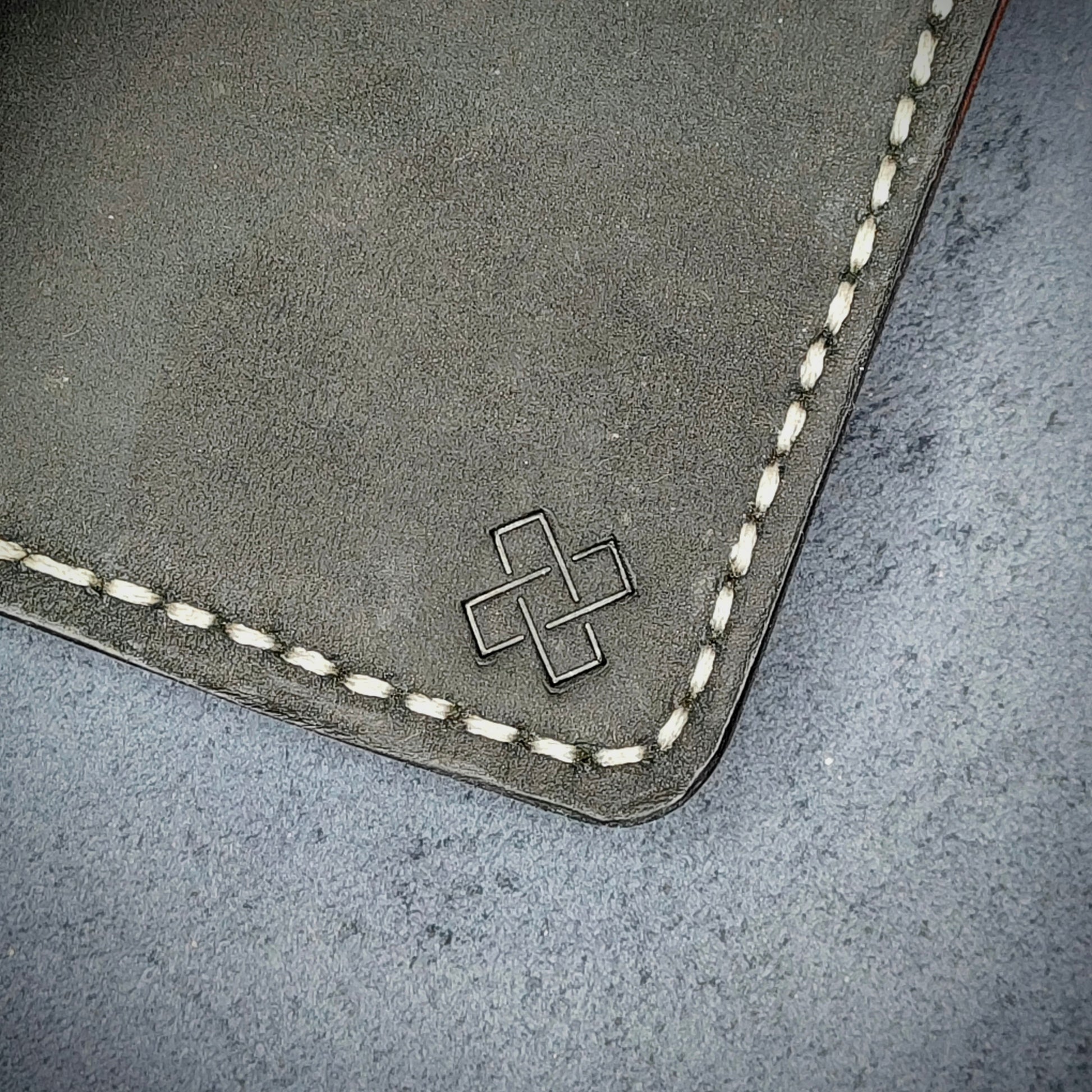 Zoomed in view of Novelty Atelier’s signature insignia embossed on The Copperfield minimalist leather card holder. Hand stitched in off white thread using traditional saddle technique. Crafted from full grain Black and Purple leather, symbolizing timeless durability and ethical sophistication.
